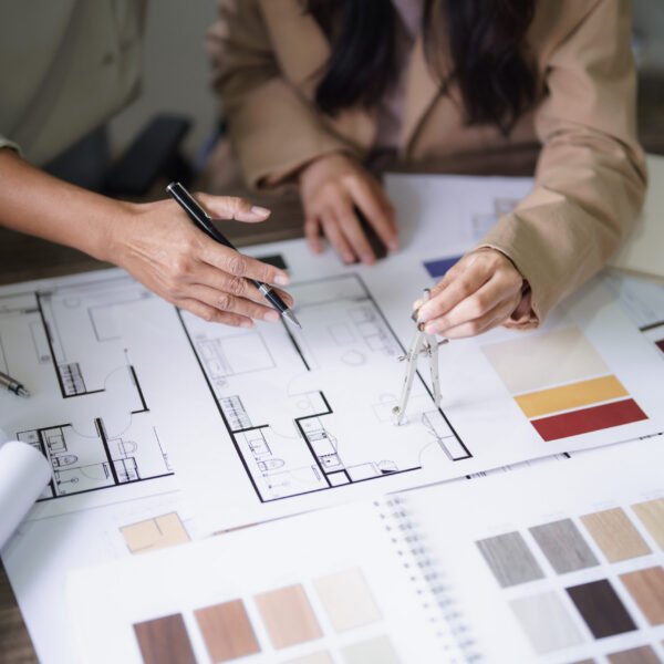 Two female architects discuss interior design building project and use divider compass on blueprint.